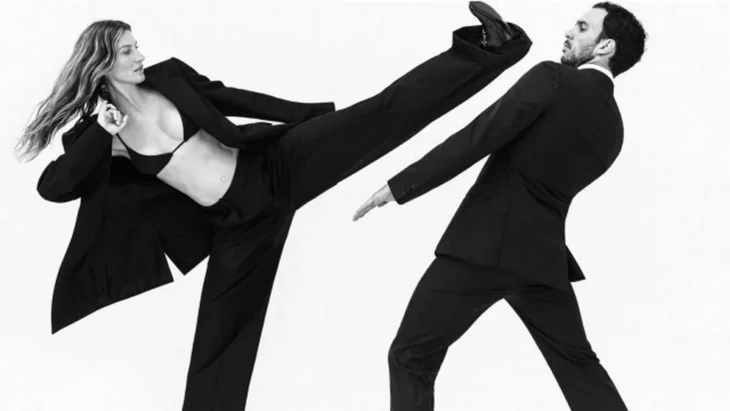 una mujer simulando dar una patada a un hombre ambos estan vestidos con trajes elegantes en color negro