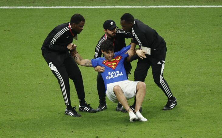 Three security guards at a stadium in Qatar 2022 removing a fan from the playing field in a World Cup match 