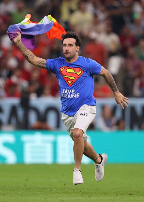 Fan running through the pitch of a football stadium with a flag of the LGBT community 