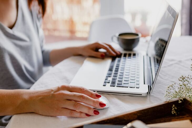 Laptop on a table and woman with hand on keyboard and mouse doing home office