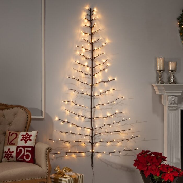 ramas secas en forma de árbol de navidad decorado con luces pegados en la pared de una casa 