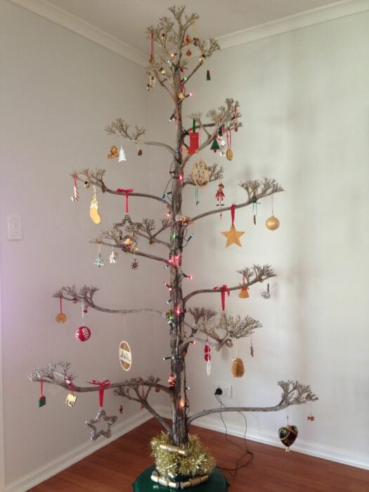 árbol de navidad con ramas secas decoraco con estrellas, esferas, bastones y botitas navideñas de colores 