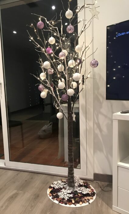 rama de árbol secas decorada con esferas en tonos lilas y luces en la sala de una casa