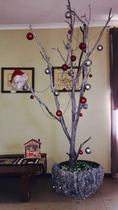árbol de navidad con grandes ramas secas decoradas con esferas rojas, plateadas y un gorro de santa 