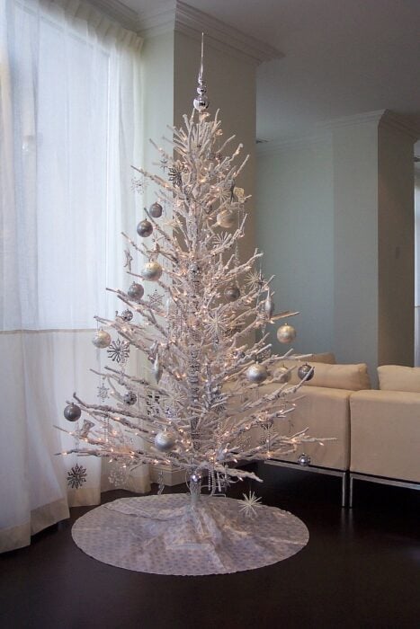 árbol de navidad seco en color blanco colocado en la esquina de una casa decorado con esferas blancas y plateadas