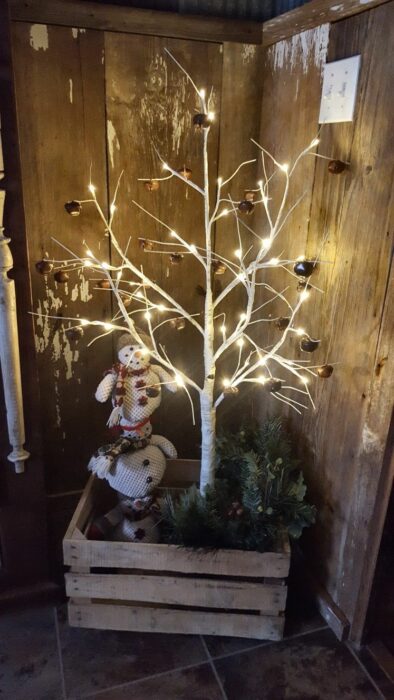 árbol de navidad hechoi con ramas secas sobre una reja de madera decorada con tres monos de nieve afilados uno encima del otro 