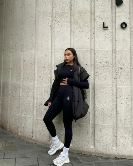 mujer posando recargada en una pared de una calle usando un coordinado negro deportivo y un chaleco oversized color negro 