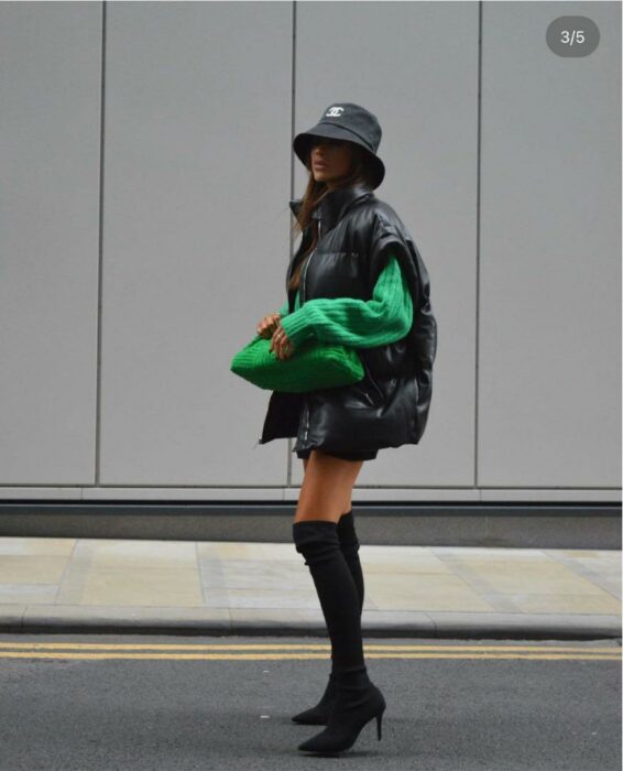 mujer posando en una calle con una botas de tacón larga un suéter color verde a juego con un chaleco oversized 