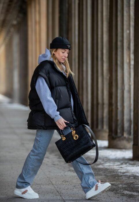 Chica posando con un chaleco oversized y una bolsa en su mano caminando por la calle 