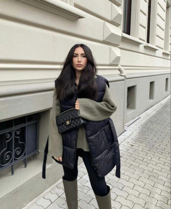 chica posando en la acera de una banqueta con un bolso en su mano a juego con un chaleco oversized en color negro 