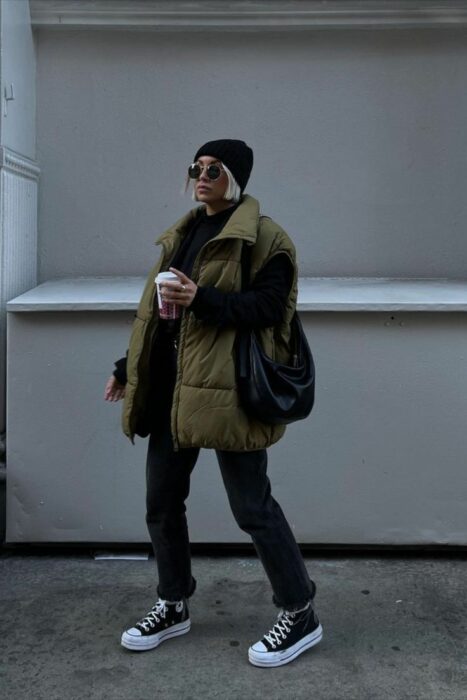 mujer posando en una calle con un café en su mano con un chaleco holgado en color verde militar 