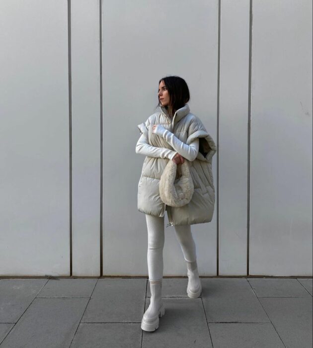 mujer vestida de blanco posando en una calle con un chaleco oversized colo blanco a juego con unas botas 