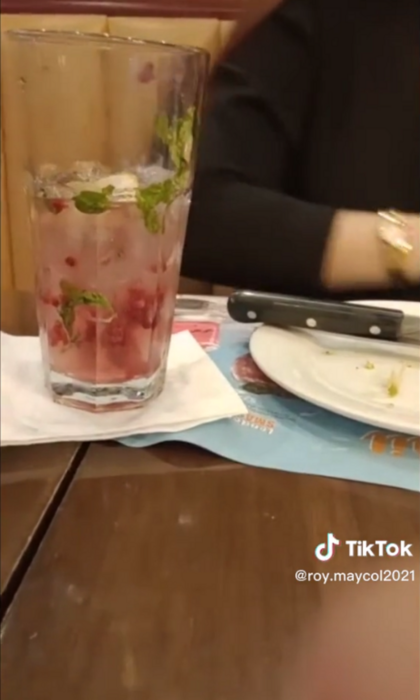 mesa de un restaurante donde estan colocados un plato sucio con cubiertos y un vaso de vidrio transparente con agua de frutas