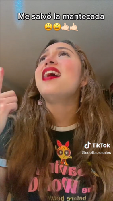 imagen de TikTok que muestra a una chica con cabello ondulado castaño señalando al cielo y con la mirada también hacia arriba lleva los labios rojos y una playera negra de las chicas super poderosas 