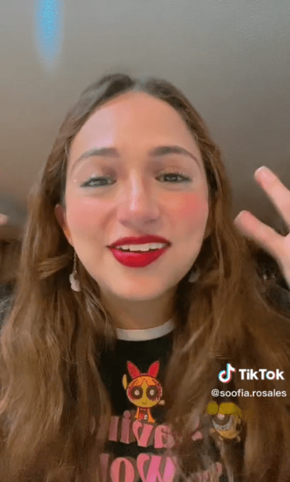 imagen de TikTok donde aparece una chica con cabello castaño largo maquillada con labial rojo lleva una playera negra alusiva a las chicas super poderosas