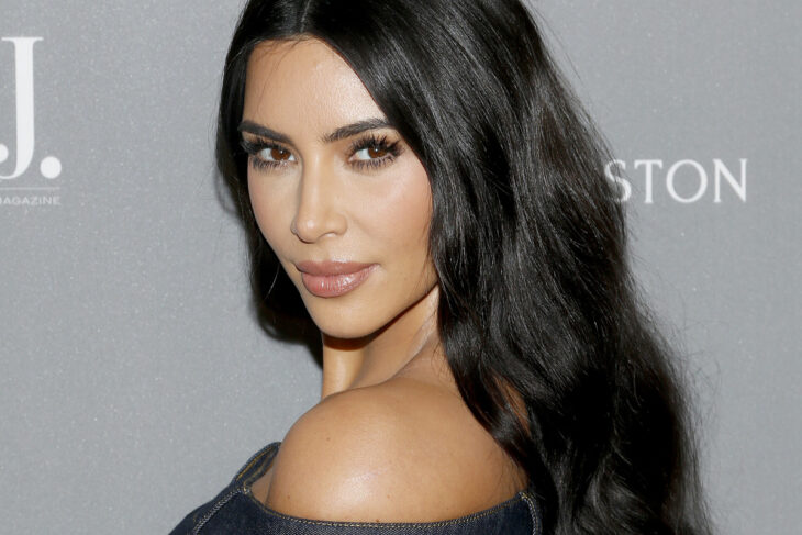 Kim Kardashian posando para la cámara lleva el cabello suelto con ligeras ondas en tono negro luce un maquillaje discreto y lleva los hombros descubiertos con un vestido negro