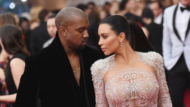 Kanye West y Kim Kardashian en una alfombra roja vestidos por Balenciaga ella lleva un vestido de pedrería en color beige y él luce un saco con camisa negra sin corbata se encuentran de semi perfil enfrente uno del otro