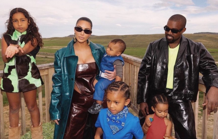 Kim Kardashian y Kanye West posando junto a sus cuatro hijos ellos van vestidos de cuero y los pequeños de manera informal están sobre el balcón de una construcción rústica en el campo