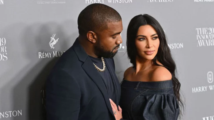 Kim Kardashian y Kanye West posando en una alfombra roja ella lleva un vestido sin tirantes negro el cabello lacio y largo maquillaje discreto él lleva un saco negro y una playera negra porta en el cuello una gargantilla gruesa de oro