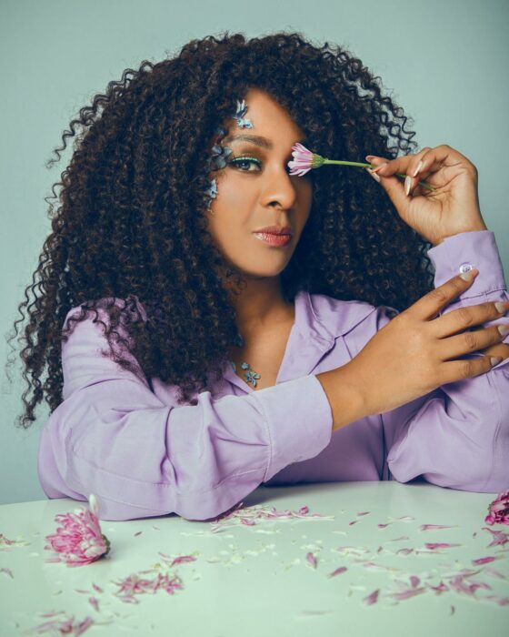 Photograph of the singer and actress M'Balia Marichal dressed in purple putting a flower in her right eye 