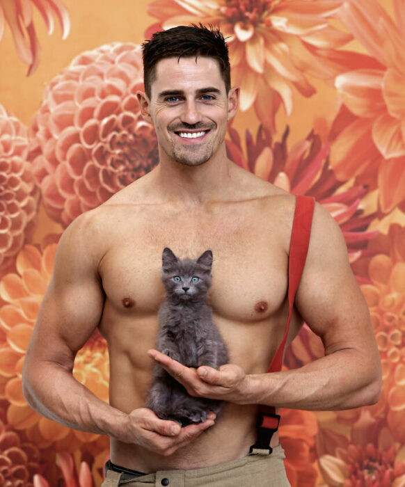 firefighter posing for charity calendar with a gray kitten in his hand
