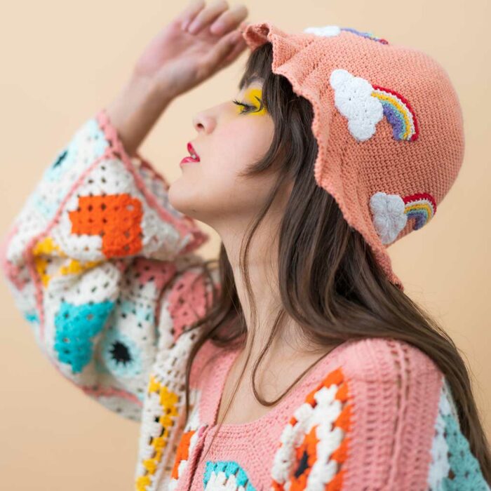 Mujer usando gorro y suéter de tejido crochet de colores con nubes y arcoíris