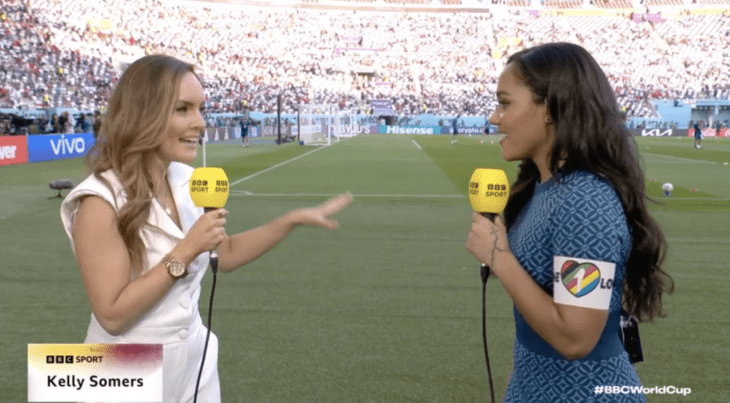 Photograph of two BBC reporters broadcasting from Qatar 2022 and one of them wearing an LGBT flag armband 