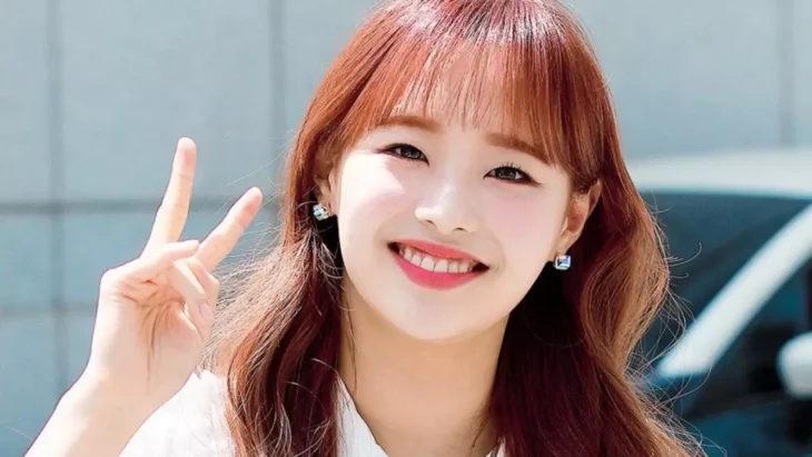 South Korean singer Chuu, former member of the K-Pop group Loona, smiles for the camera. She has loose, long reddish hair and natural makeup, wears a white blouse 