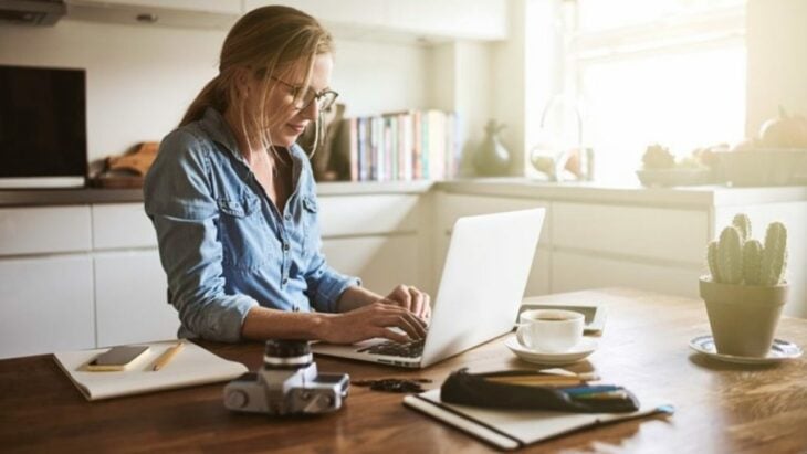 Mujer rubia con lentes sentada en una mesa utilizando una laptop