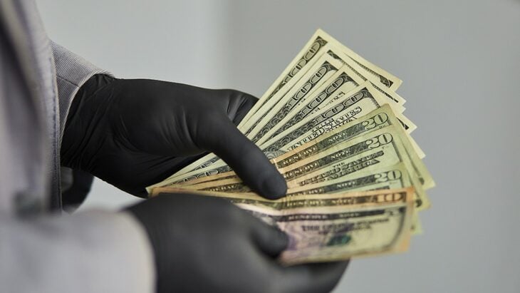 Manos con guantes negros sosteniendo billetes
