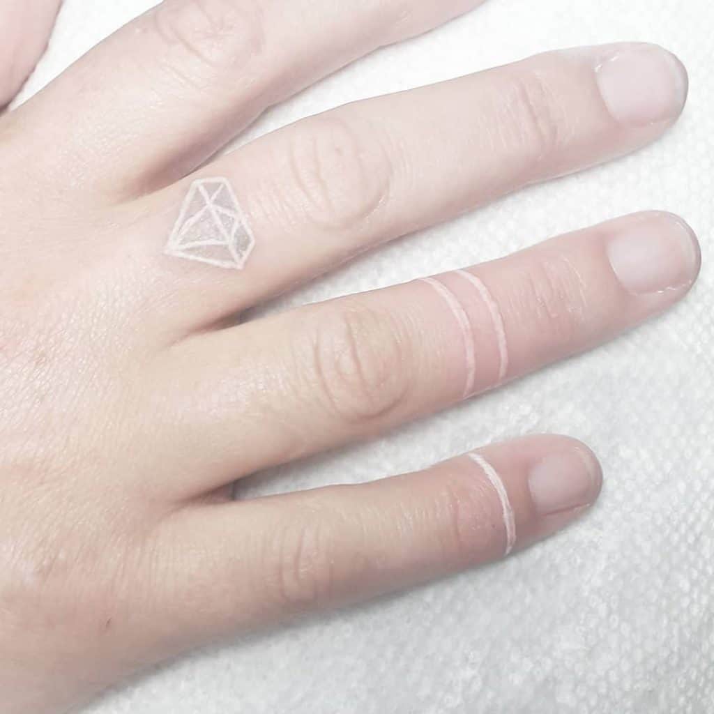 mano con tatuajes blancos simulando anillos y un diamante