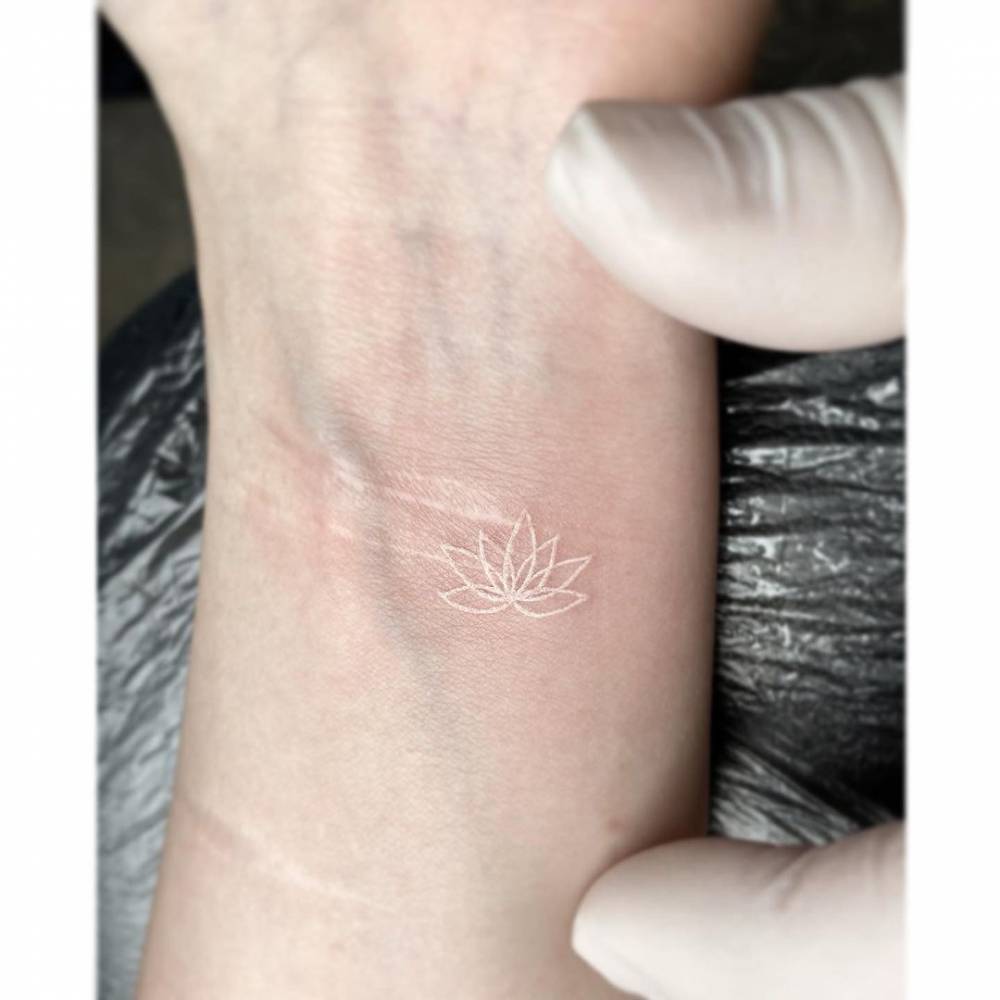 brazo de mujer con un tatuaje en color blanco con forma de flor de loto