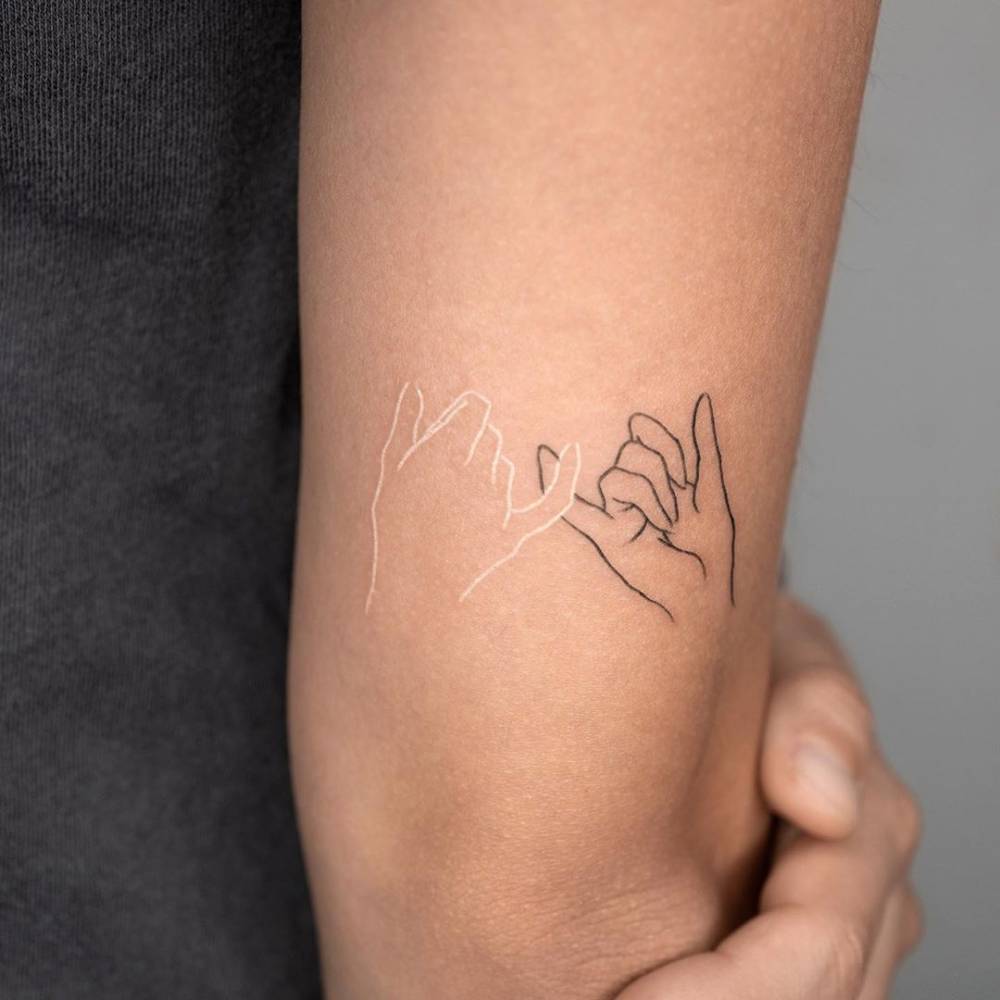brazo de mujer con tatuajes de manos haciendo promesa con el dedo chiquito