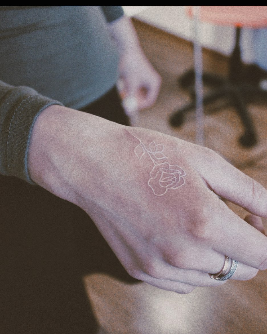 mano de mujer con tatuaje blanco en forma de rosa