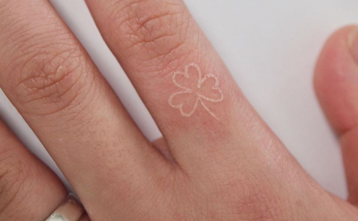 dedo de la mano con tatuaje blanco en forma de trébol