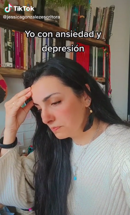 imagen de TikTok donde se aprecia una mujer con la mirada baja intentando mostrar depresión, lleva un sueter blanco y unos aretes largos negros 