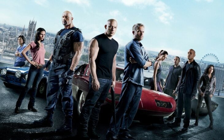 imagen promocional de la película Rápidos y furiosos aparecen los actores principales junto a los autos que conducen todos visten de manera informal