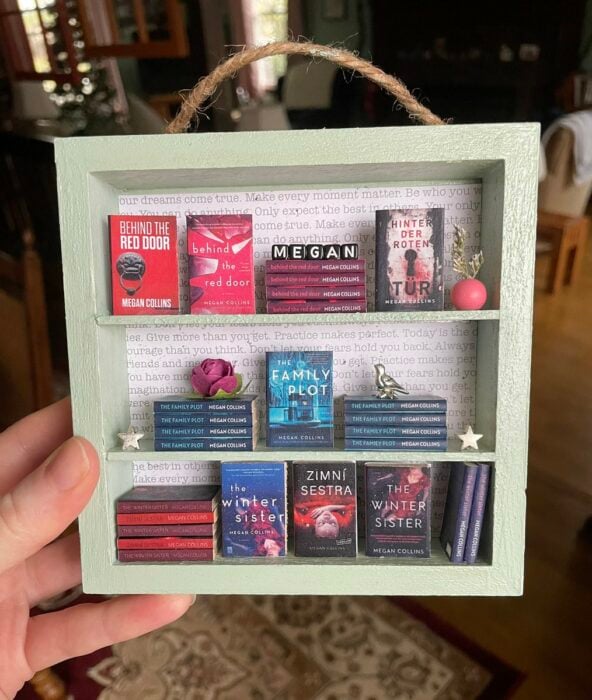mano sosteniendo un mini estantes con libros en miniatura 