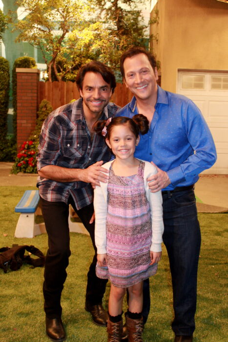 Jenna Ortega junto a Eugenio Derbez y otro actor posando en una imagen la niña lleva un vestido rosa estampado y un suéter blanco