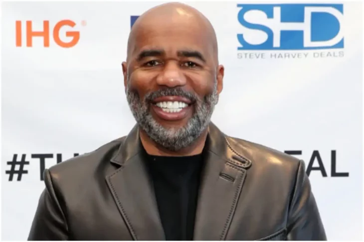 Steve Harvey sonriendo en la imagen lleva un saco de cuero gris y una playera negra lleva la barba crecida y canosa 