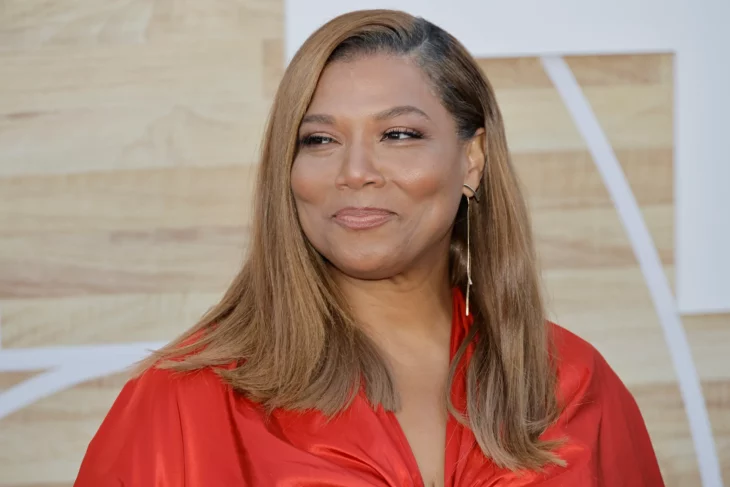 Queen Latifah sonriendo en la imagen lleva un vestido rojo y el cabello castaño y largo medio lacio su maquillaje es discreto