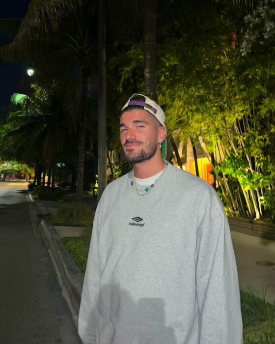 Rodrigo de Paul con sudadera gris y gorra hacia atrás de pie en la calle