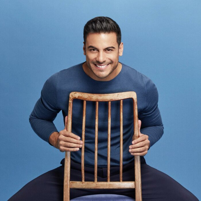 Carlos Rivera sentado en una silla con fondo azul