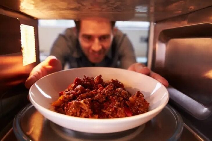 Hombre calentando comida en el horno de microondas 