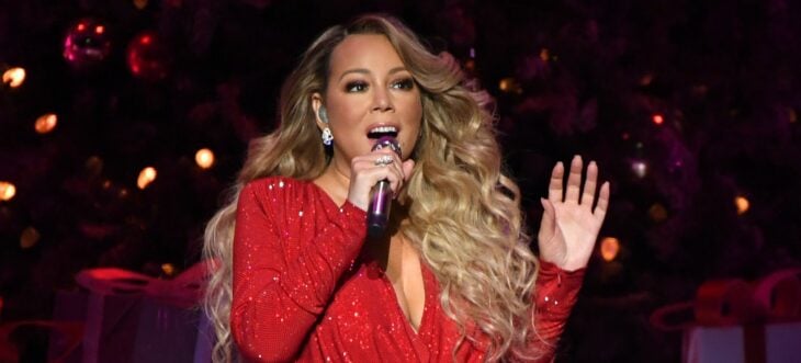 la cantante Mariah Carey durante una presentación navideña lleva un vestido de noche rojo luce el cabello suelto peinado con ondas tare un micrófono en la mano y está interpretando un tema