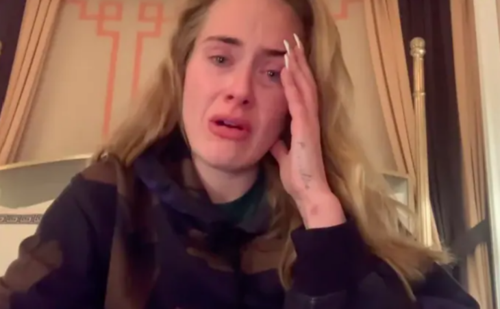 La cantante Adele hablando para la cámara visiblemente consternada se nota que está llorando no trae maquillaje y lleva el cabello suelto trae una sudadera de color negro y uñas postizas en tono blanco