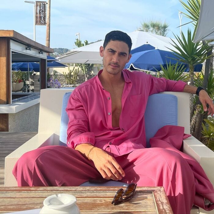 Alejandro Speitzer con un conjunto rosa sentado en un sillón en la playa 