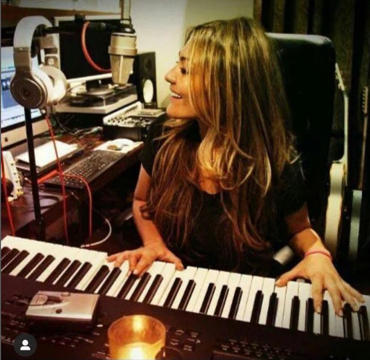 Amaia Montero en su estudio de grabación está tocando un teclado y sonríe lleva ropa casual y el cabello suelto y largo rubio