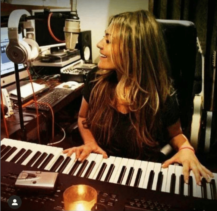 Amaia Montero en su estudio de grabación está tocando un teclado y sonríe lleva ropa casual y el cabello suelto y largo rubio