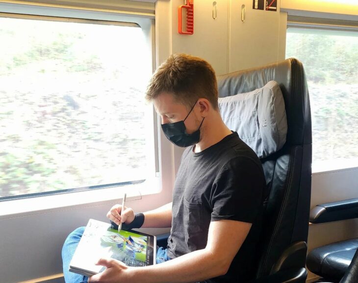 Fotografía de un chico dibujando sentado en el asiento de un vagón de un tren 